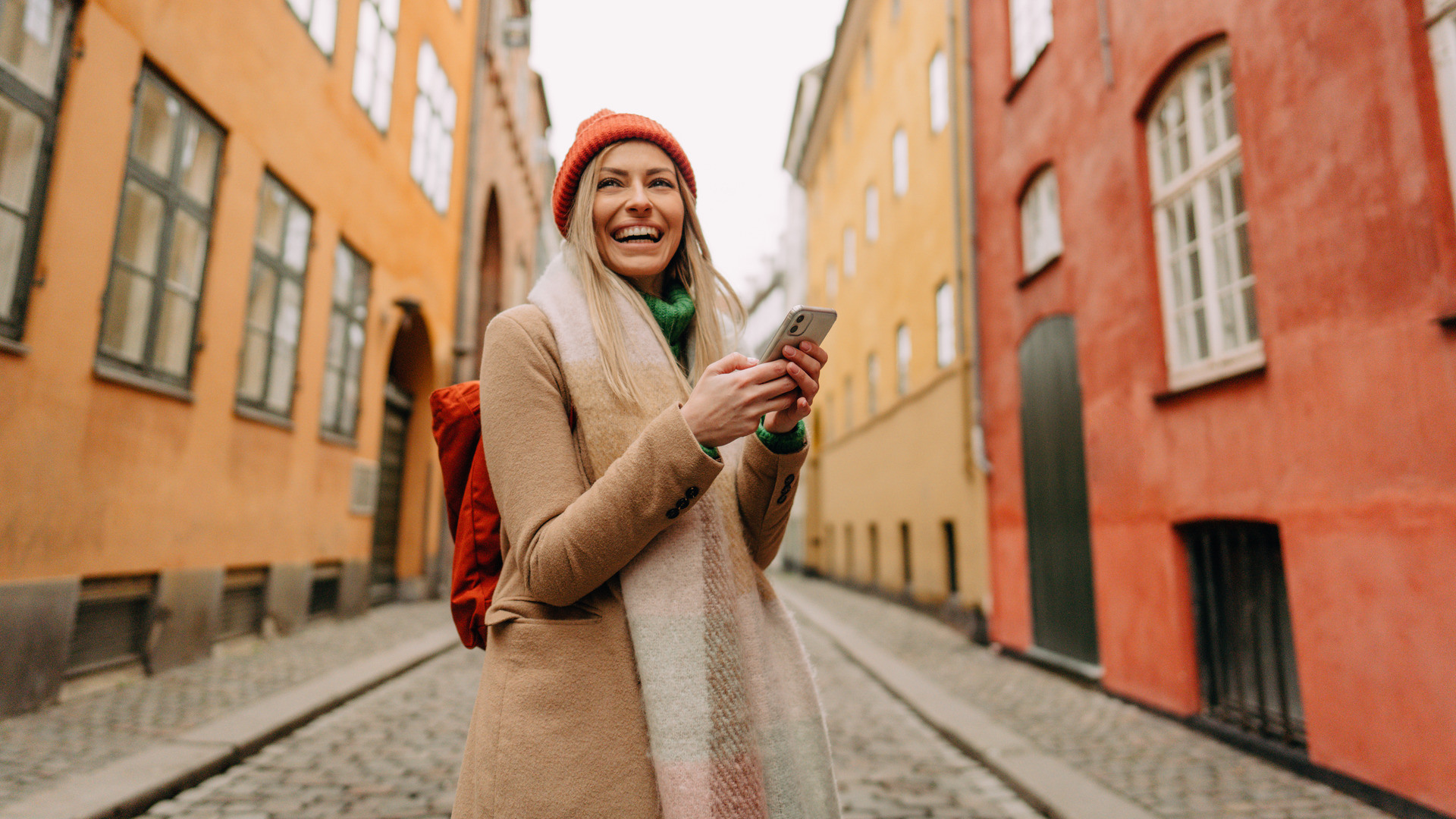 En ung dame som står på gaten og holder en mobiltelefon i hånden