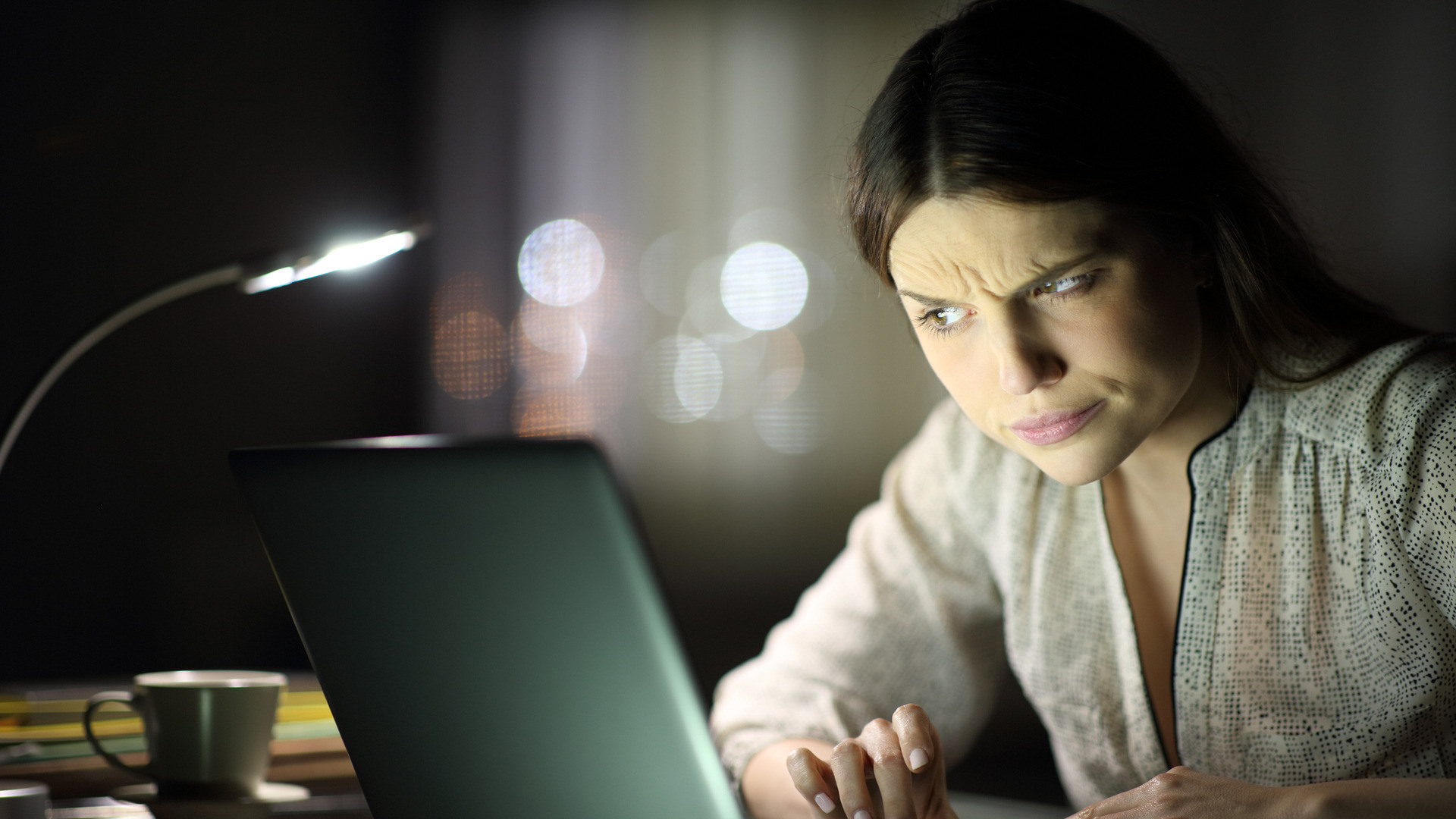 Kvinne i mørkt rom ser veldig skeptisk på et opplyst PC